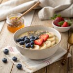 A bowl of porridge topped with fresh fruits like blueberries, strawberries, and banana slices, drizzled with honey and sprinkled with chia seeds.