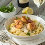 A bowl of shrimp pasta with seared shrimp, creamy sauce, fresh parsley, and grated Parmesan, served with a lemon wedge and white wine.