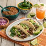 Beef tacos with seasoned meat, fresh toppings, and a side of guacamole and salsa.