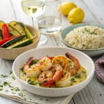 Garlic shrimp served with herbed rice, grilled vegetables, and white wine on a rustic wooden table.