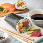 "A sliced sushi burrito showcasing colorful tuna, avocado, cucumber, and rice, served with chopsticks and soy sauce on a clean background."